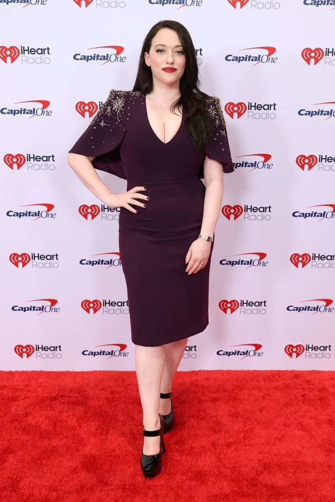 Frontal view of Kat Dennings posing on a red carpet with one hand on her hip