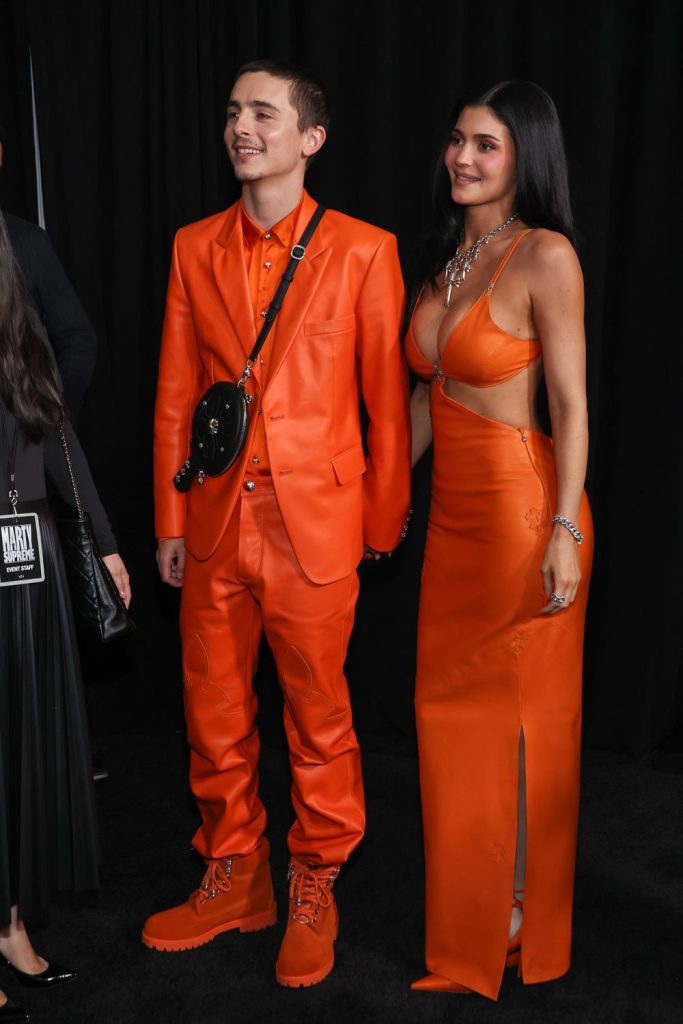 Frontal view of Kylie Jenner and Timothée Chalamet wearing matching outfits and waiting to step onto a red carpet