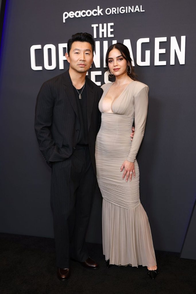 Full body frontal of Melissa Barrera posing next to an Asian man