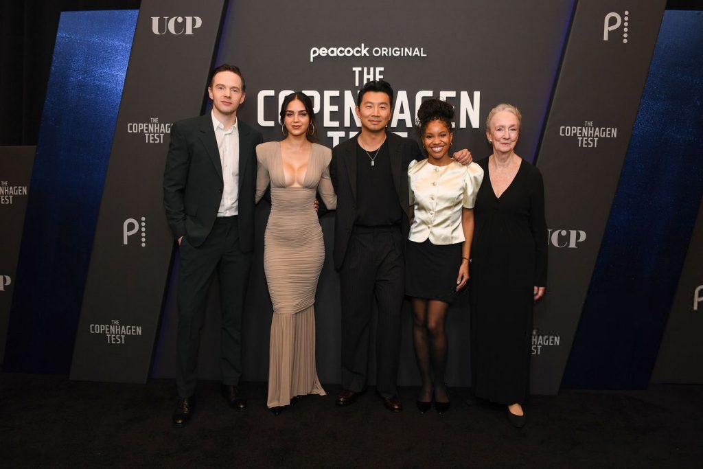 Far away frontal of two men and two women posing on a red carpet next to each other