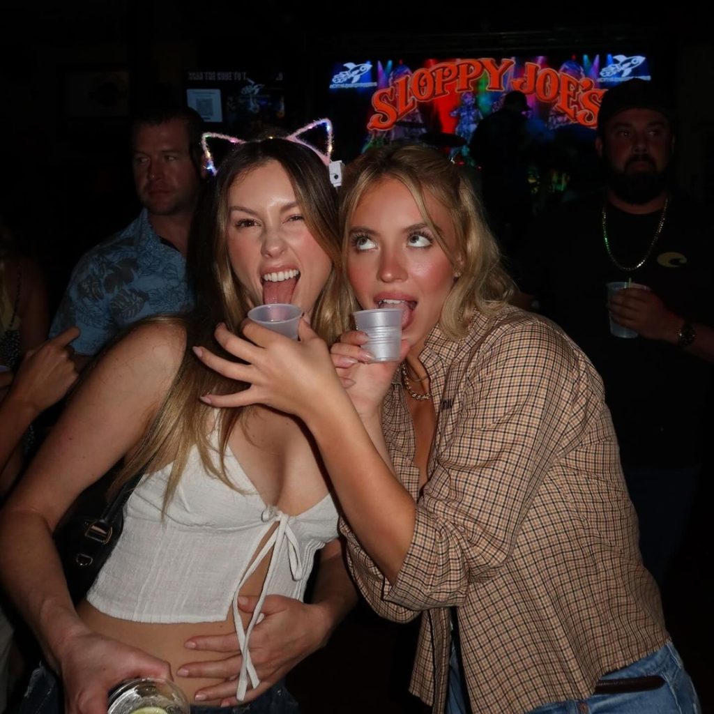 From waist up frontal view of two girls sharing shots at a party