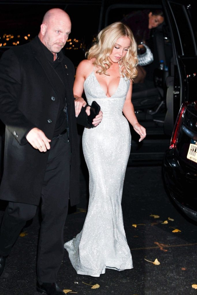 Full body front view of a big man helping Sydney Sweeney out of a car