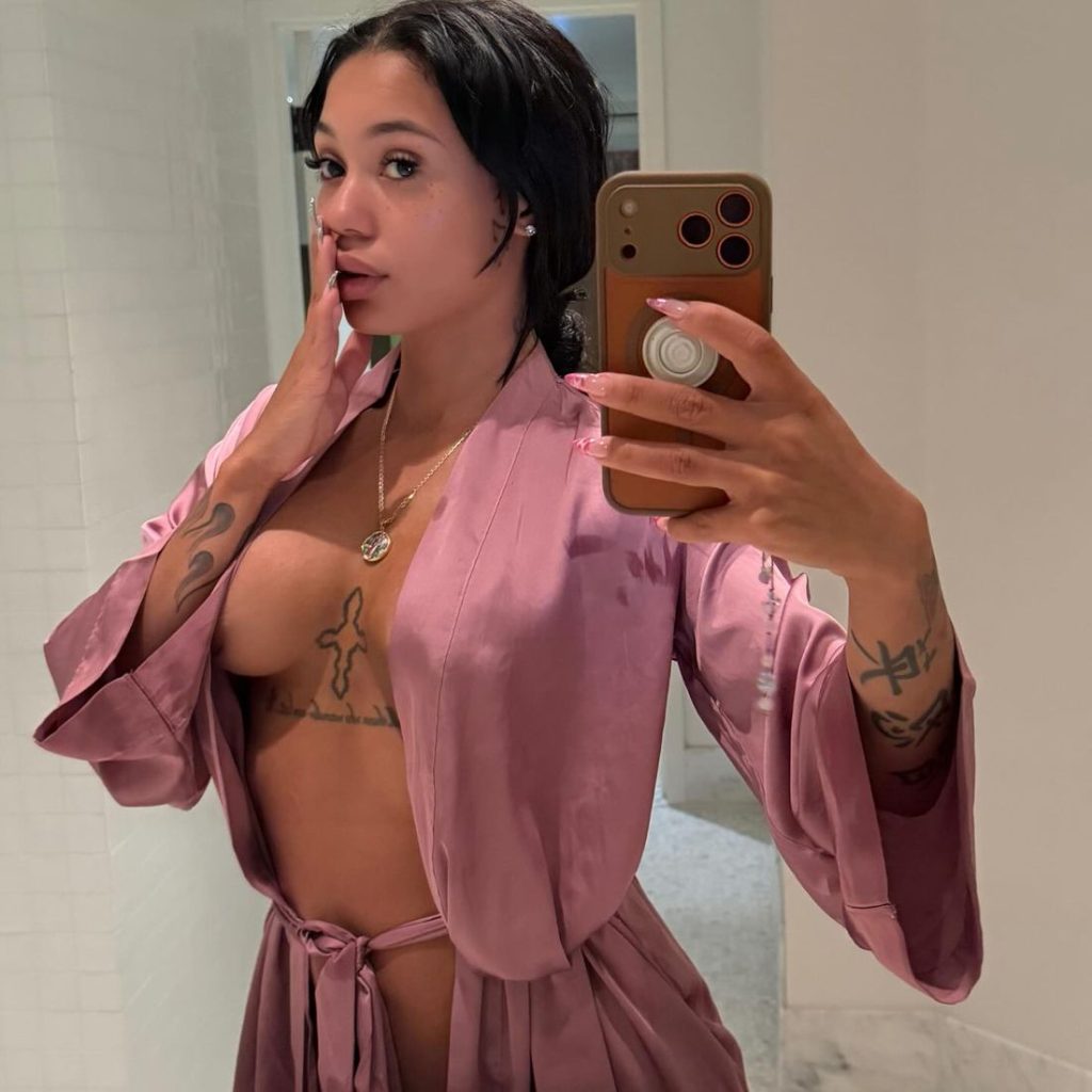 Side frontal view of Coi Leray snapping a selfie in an open robe to show off her new breast implants