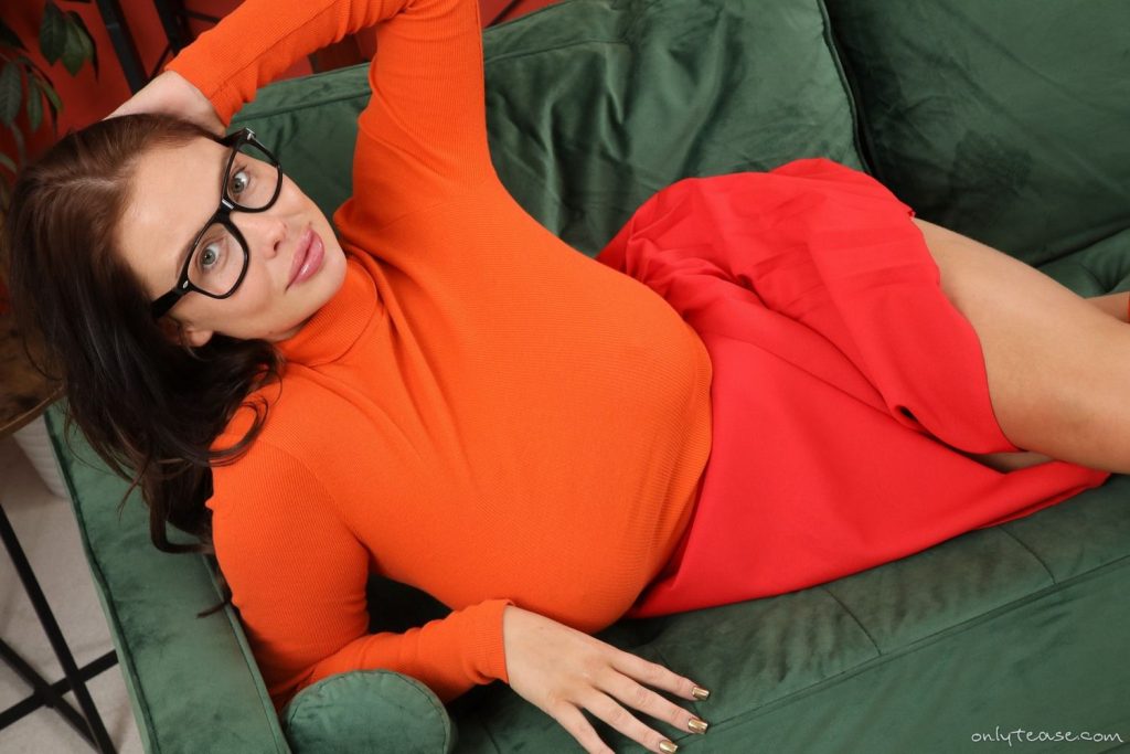 Woman dressed as Velma laying down on her side on a couch