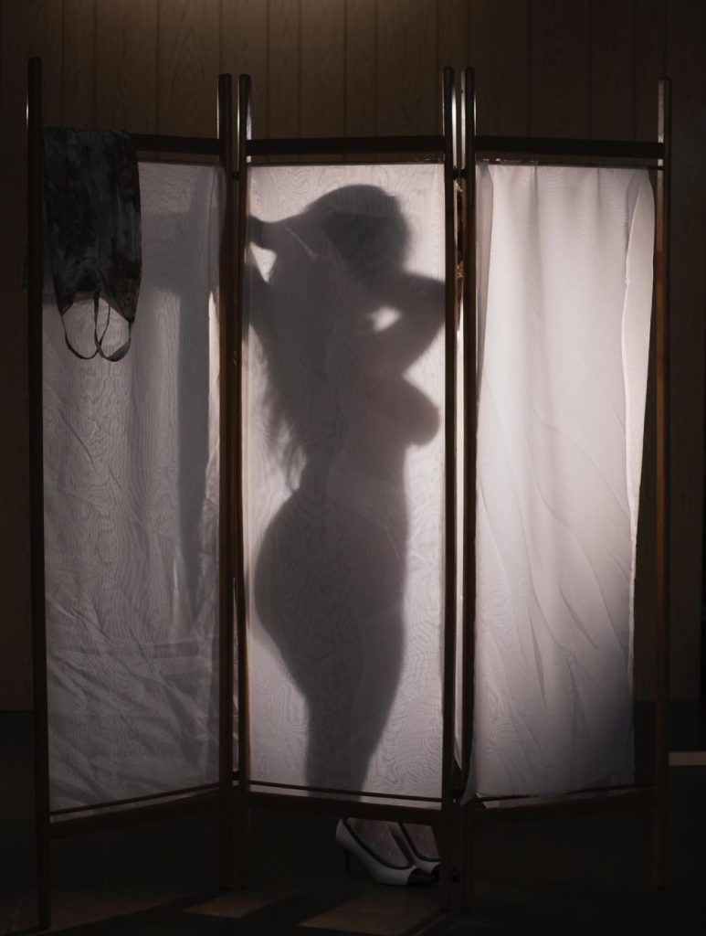 Silhouette of a nude and curvy woman behind a sheet