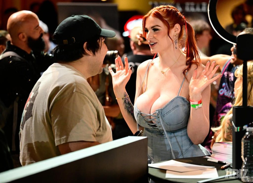 Side view of porn star with huge breasts interacting with a fan