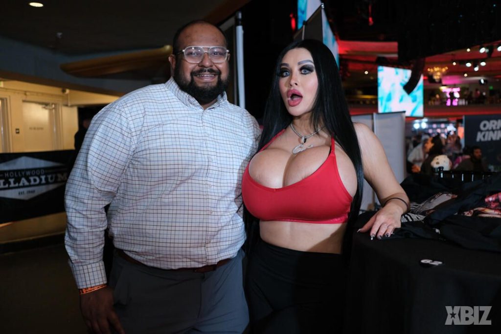 Frontal of porn star with huge fake breasts posing next to a fan