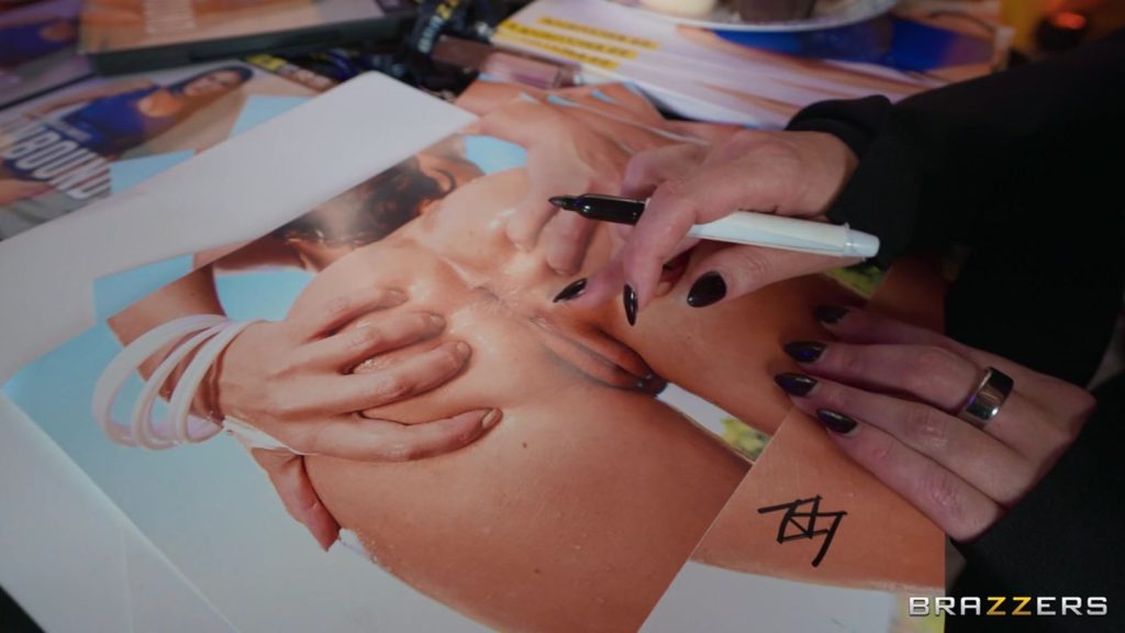A woman's hand holding a pen as she's about to sign an explicit poster of a woman's vagina.
