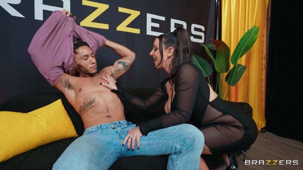 Angela White squatting down and touching a man's chest as he removes his shirt.