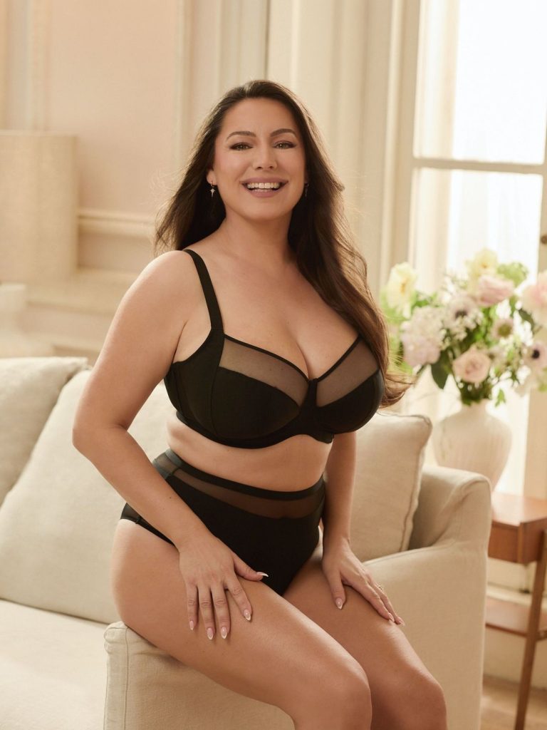 Frontal of woman wearing underwear, sitting on the arm rest of a sofa with a big smile