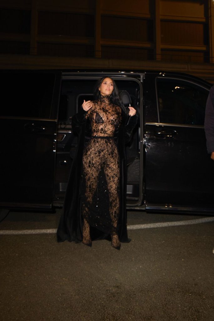 Far away view of Kim Kardashian standing outside a car wearing lace and a coat