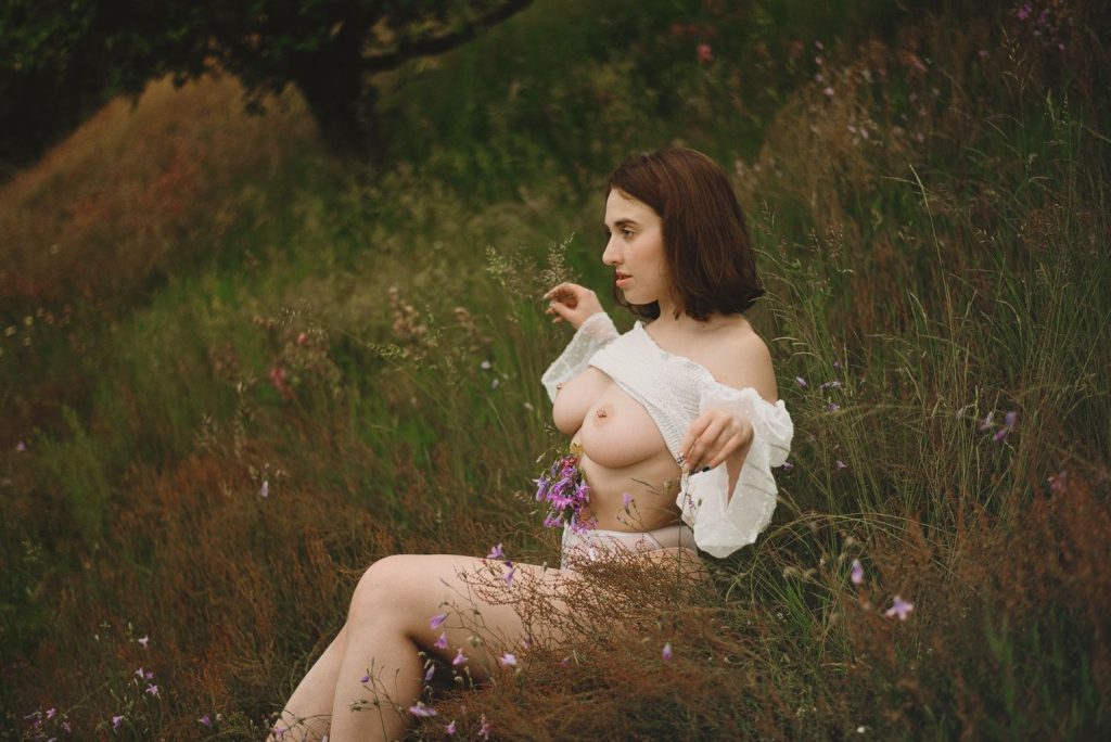 Sideways view of redhead sitting in the grass and lifting her top up to show her breasts