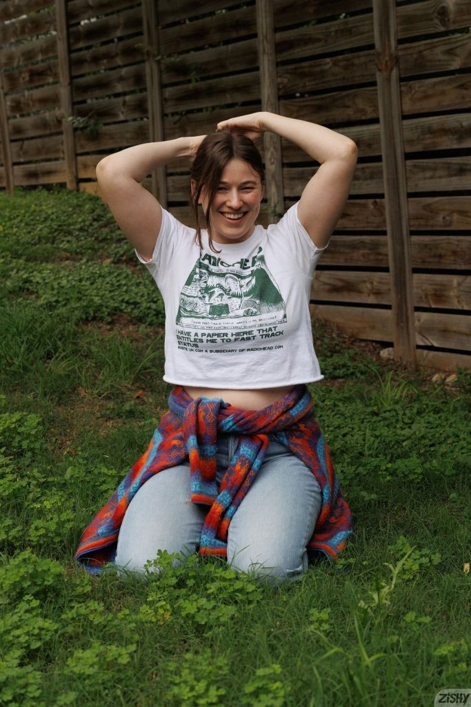 Frontal of smiling girl siting on her knees in the grass with arms on top of her head