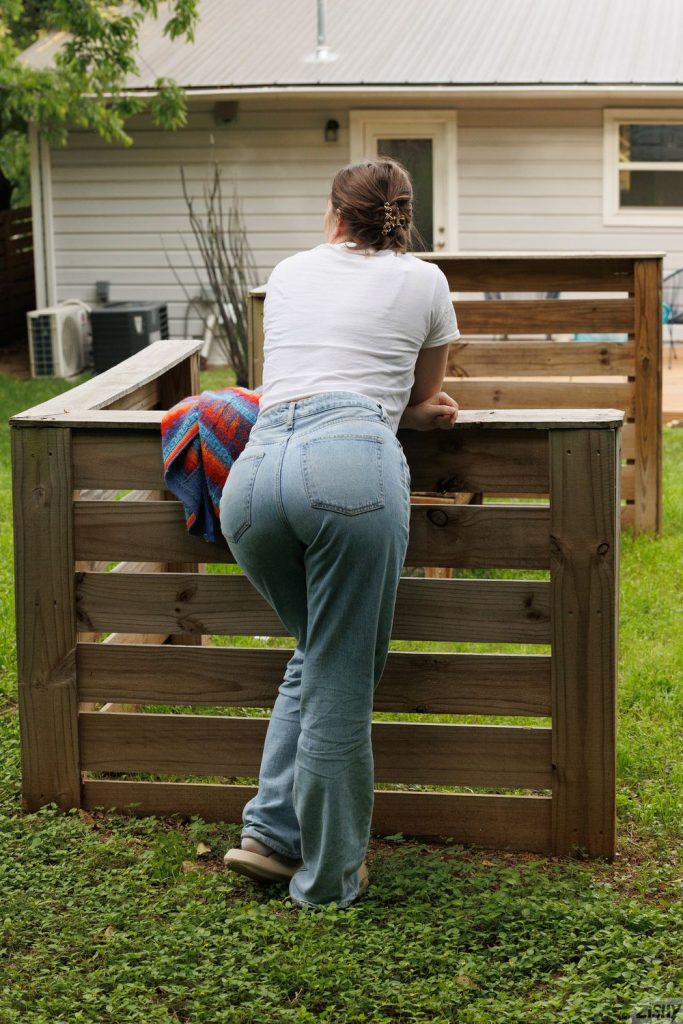 Full body backside view of girl wearing denim and leaning against a wood fence