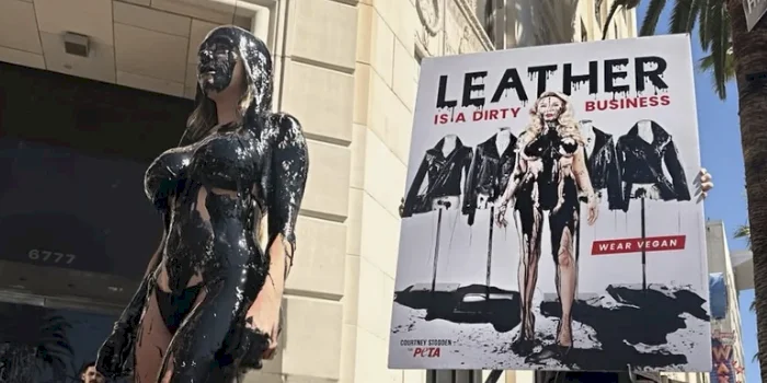 A woman standing on a public sidewalk wearing a bikini and drenched from head to toe with a thick black substance.