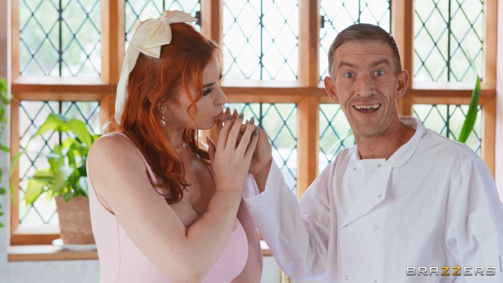 A redhead woman sucking on the finger of a man wearing a chef's coat. He looks at the camera with a delighted expression