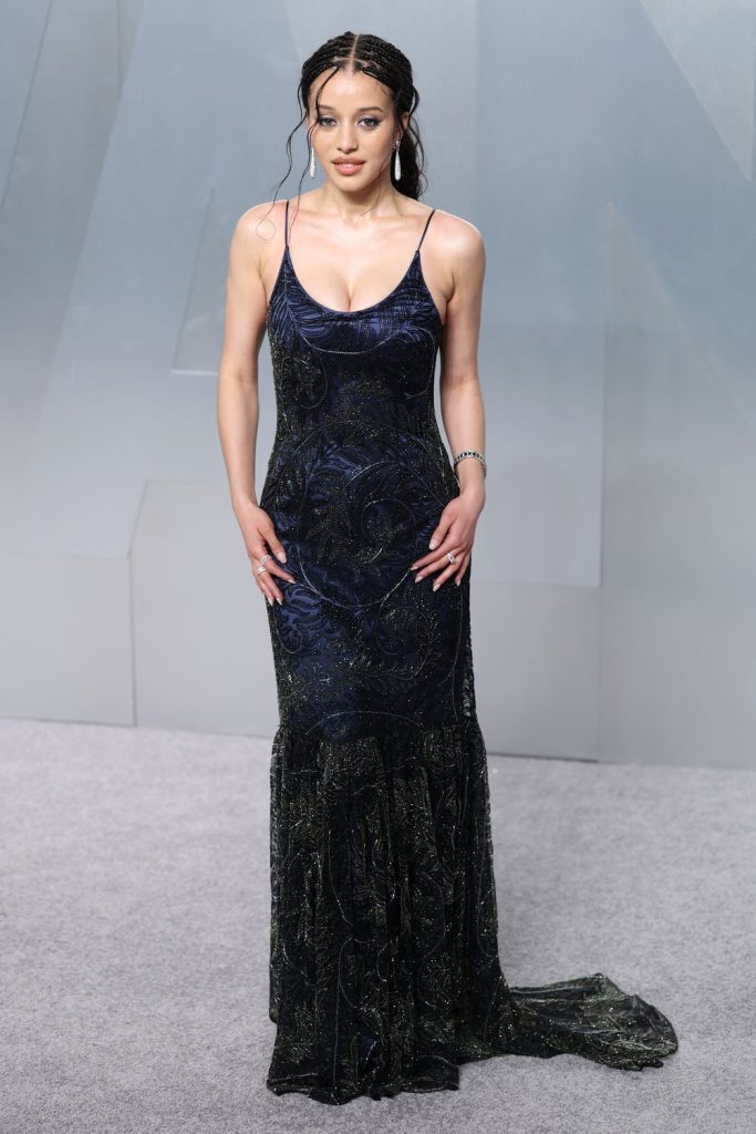 A girl wearing a long dark blue dress with a black feather pattern against a light grey background