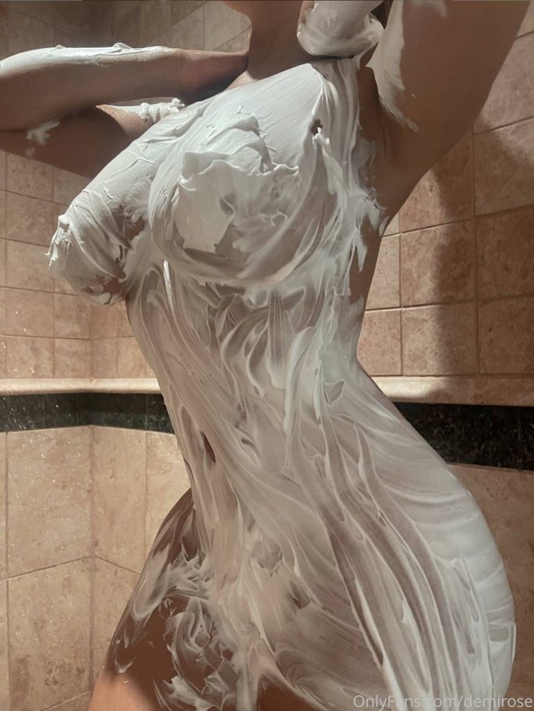 A person standing in a tiled shower, their body covered in thick, white foam or shaving cream, with their face out of frame.