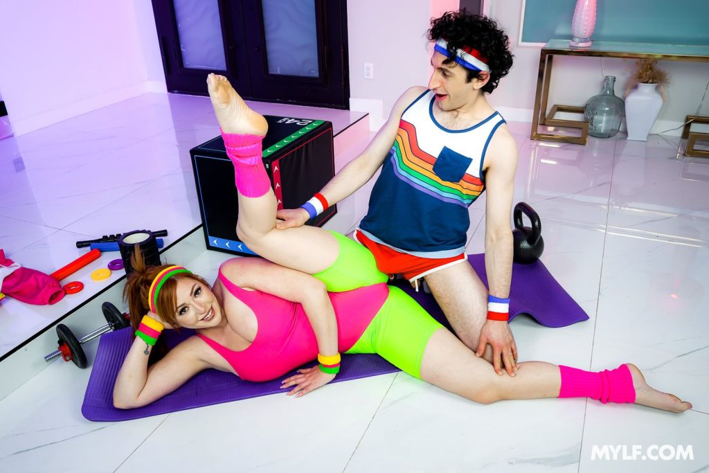 A woman wearing neon clothing is lying on her side with her legs in a split. A goofy guy wearing speedos is putting his crotch towards her crotch.