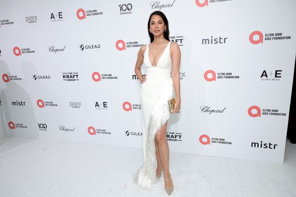 Brunette woman in a white dress in front of a white background with logos.