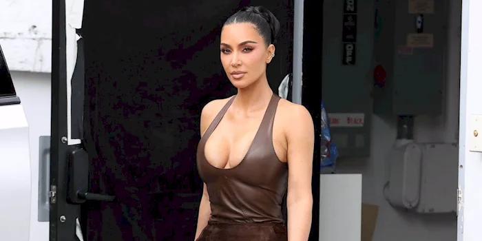 Kim Kardashian walks outside wearing a brown leather dress