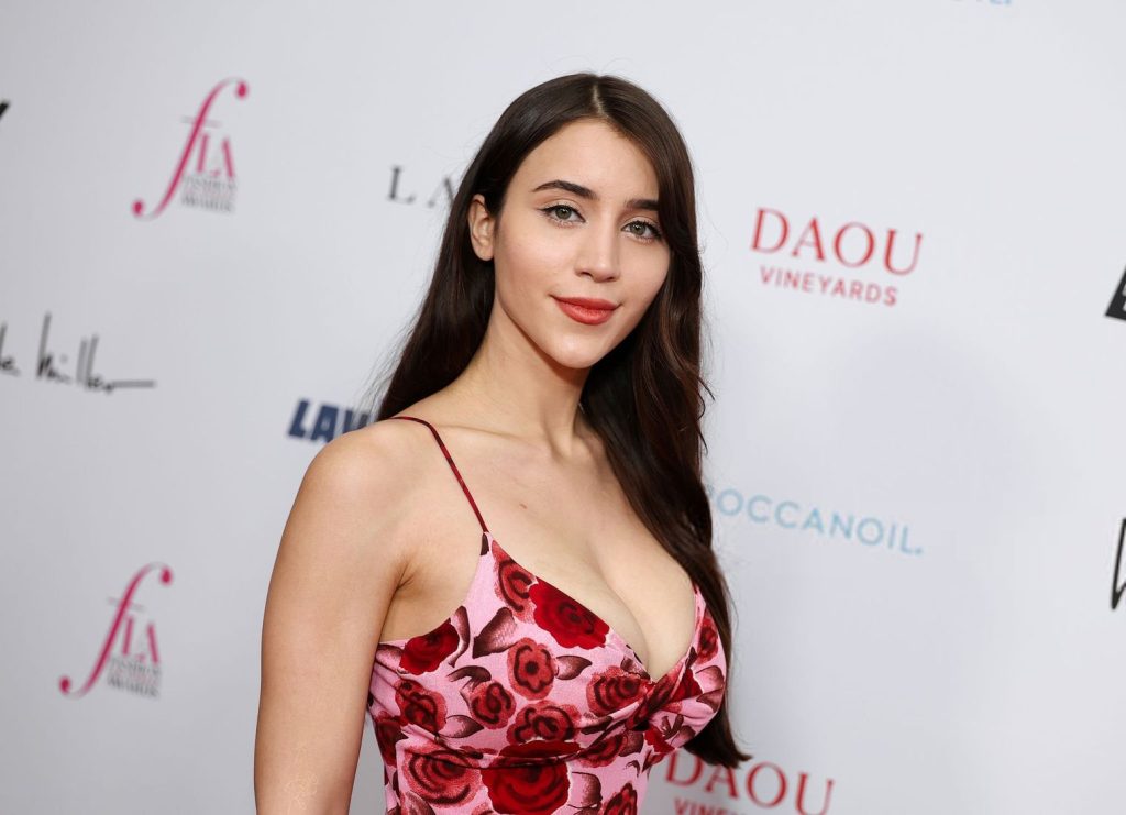 Close up side view of a woman with long dark hair in a pink and red floral dress smiling.