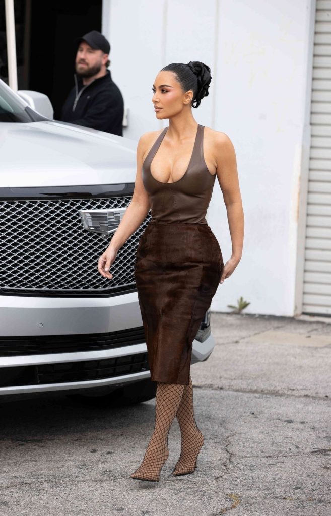 Kim Kardashian walking outside near a silver vehicle, with a man standing in the background.