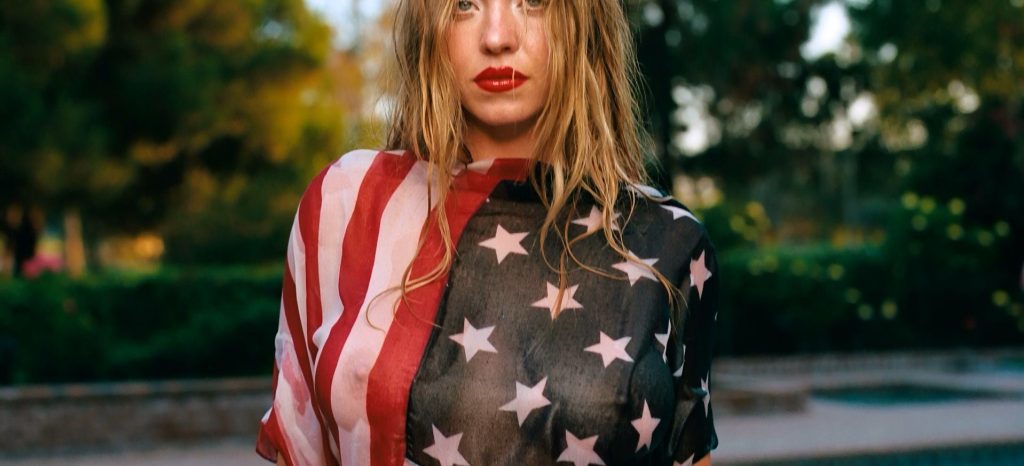 Close up of Sydney Sweeney braless and wearing a sheer top of the American flag.
