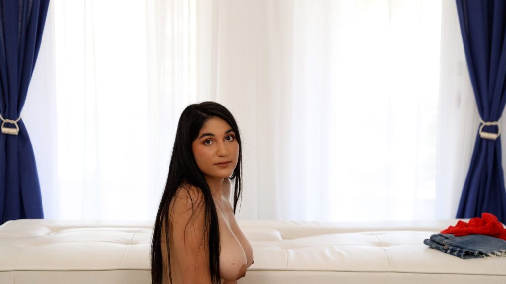 Profile view of a topless brunette girl turning her head and looking into the camera.