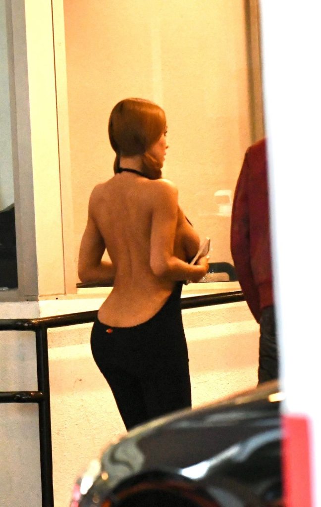 A woman, seen from behind, wears a black dress with a very low back. She holds a phone in her right hand.