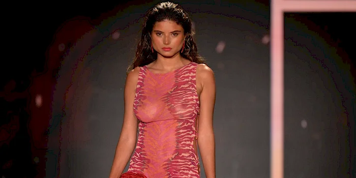 Close up of model walks down a runway wearing a see through, form-fitting, sleeveless pink dress.
