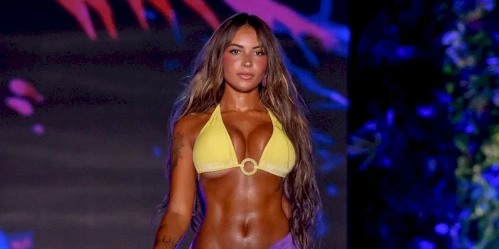 Close up of a woman walks on a runway wearing a yellow bikini top.
