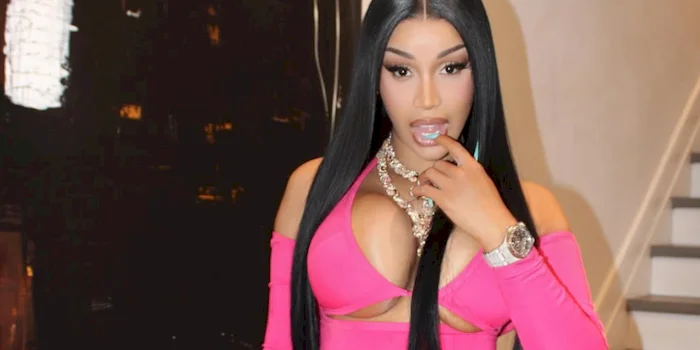 Cardi B wears a bright pink cut-out top. putting one finger up to her lips.