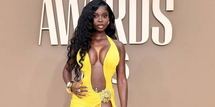 Black woman in a bright yellow, flowing gown poses on the BET Awards red carpet. The dress features a high slit and deep neckline.