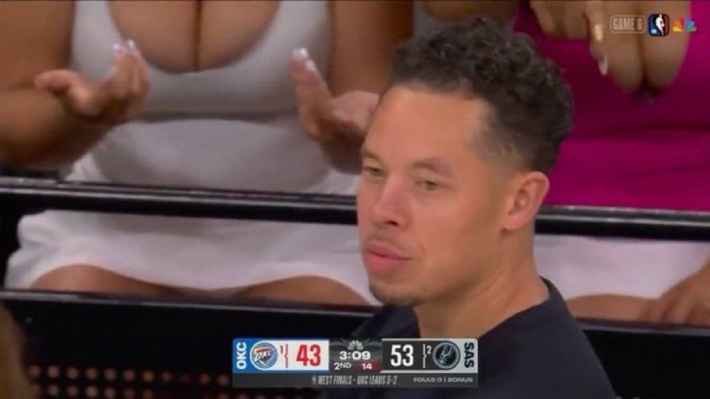 A man with short curly hair sits in the crowd at an NBA game, looking thoughtful. The game score shown reads OKC 43, SAS 53, with 3:09 left in the second quarter. Fans’ hands are visible in the background.