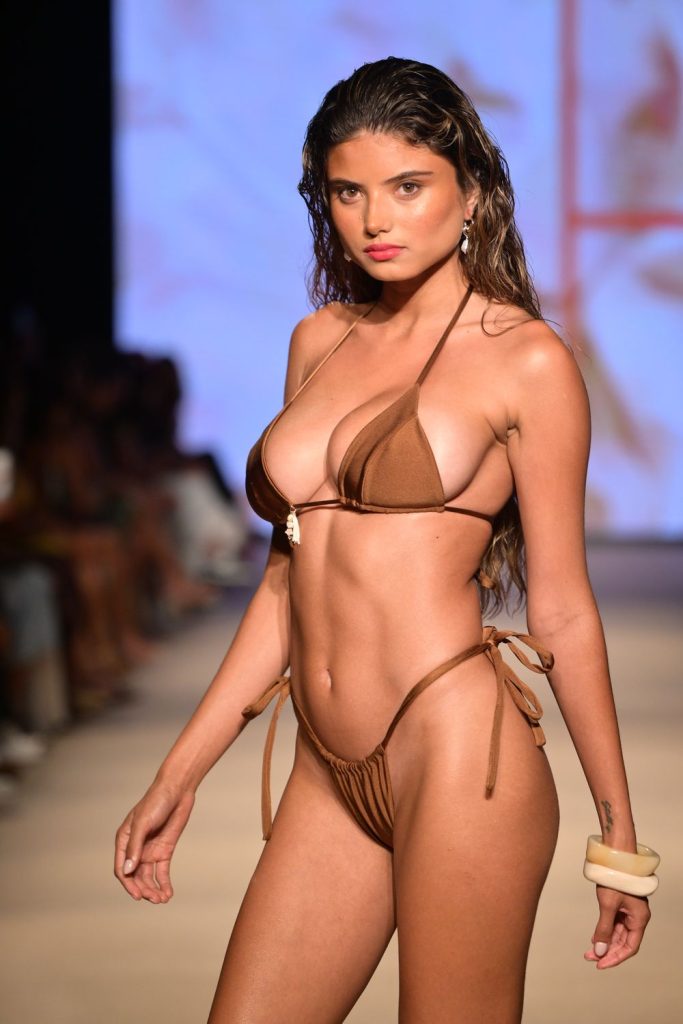 Model posing at a side angle on the runway, wearing a brown bikini.