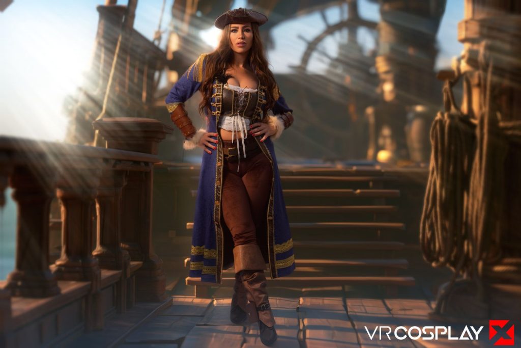 A woman in a blue pirate costume stands on a wooden ships deck, sunlight streaming through the rigging. She wears a hat, long coat, brown pants, and boots.