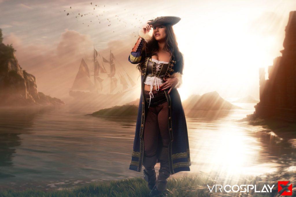 A woman in pirate cosplay stands by the water at sunset, wearing a tricorn hat and long coat. Tall ships sail in the background, with cliffs and birds silhouetted against the glowing sky.