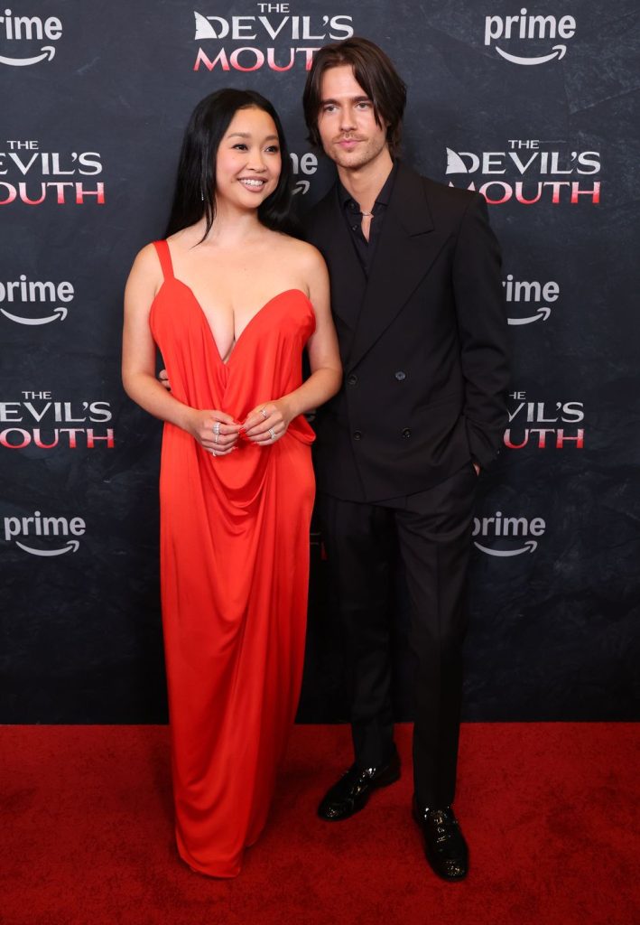 A woman in a red gown and a man in a black suit pose together on a red carpet at a premiere event for The Devils Mouth, with branded backdrops and the Prime logo behind them.
