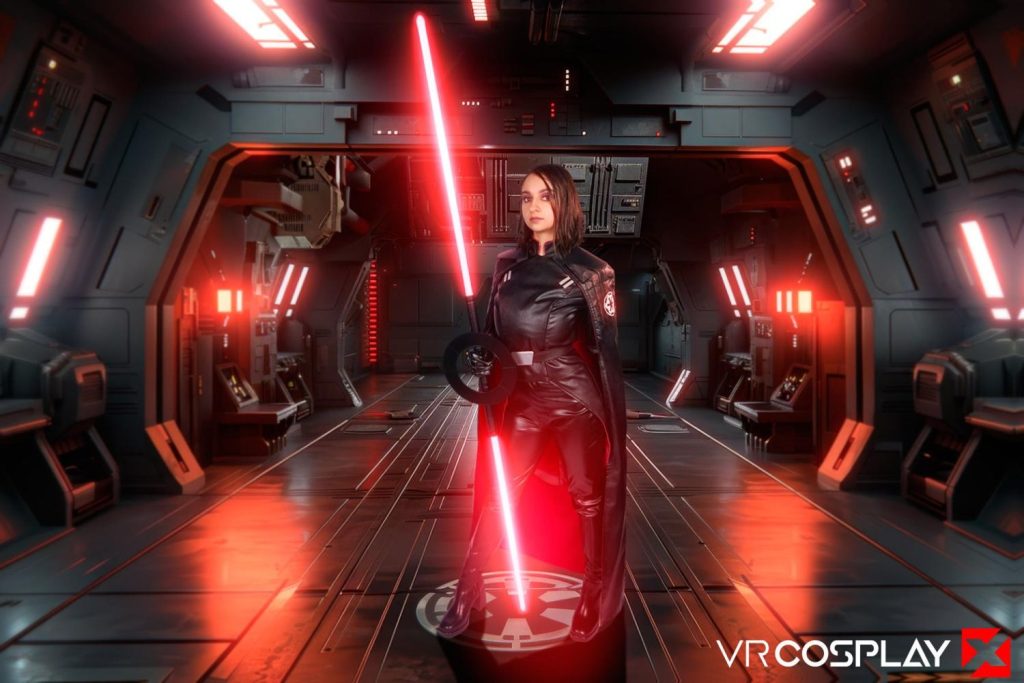 Woman with dark hair in a black leather bodysuit and red cape holding a red lightsaber, standing in a sci-fi corridor.