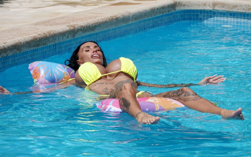 A woman in a yellow bikini floats on a colorful pool lounger in a swimming pool, relaxing with her eyes closed and arms and legs spread out.
