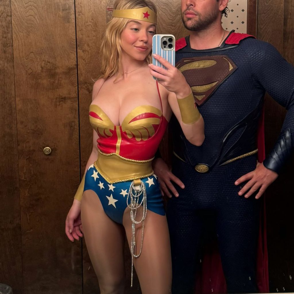 A woman in a Wonder Woman costume and a man in a Superman costume take a mirror selfie together in a wood-paneled room.