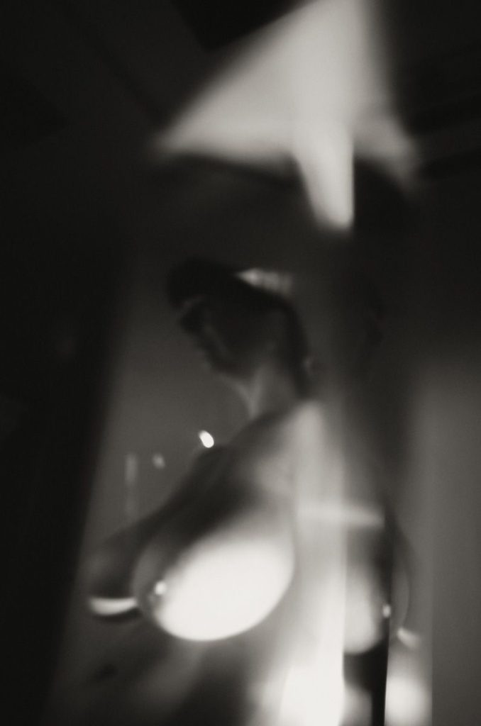 A blurred, black-and-white image showing an abstract, partially obscured figure with soft lighting and strong contrasts, creating a mysterious, artistic effect.