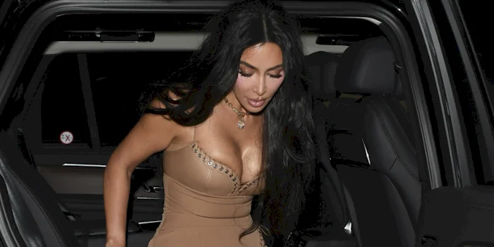 Close up of Kim Kardashian exiting a car wearing a tan, form-fitting dress.