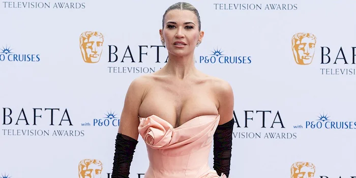 Christine McGuinness in a strapless peach-colored bodice and a black skirt with long black gloves poses in front of a BAFTA Television Awards step-and-repeat backdrop.