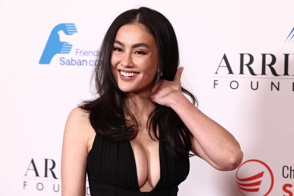 Asian woman with full wearing a black plunging halter-neck gown smiles while touching her hair.