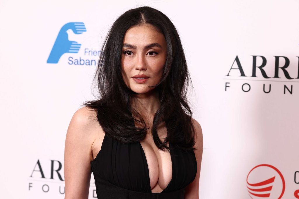 Asian woman with full wearing a black plunging halter-neck gown looks at the camera with a neutral expression.
