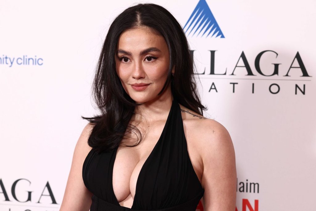 Asian woman with full breasts wearing a black plunging halter-neck gown looks slightly to the side.