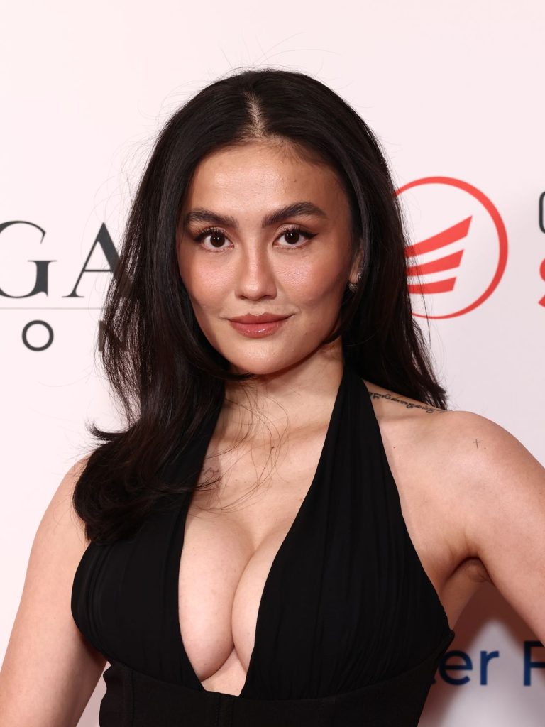Close-up of a Asian woman with full breasts wearing a black plunging halter-neck gown looking at the camera.