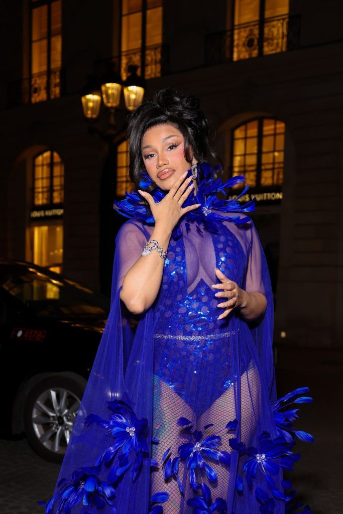 Cardi B wearing a sheer royal blue bodysuit and cape adorned with feathers.